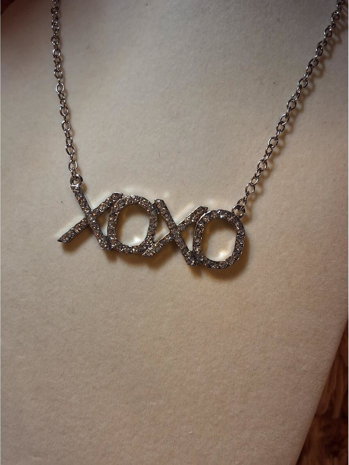 XOXO Jewelry Ideas: 10 Ways to Wear These Timeless Symbols 2 Silver XOXO pendant necklace with crystals displayed on a beige jewelry bust